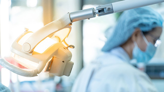 Close up of dental operatory light in dental clinic, a dentist in the background Close up of dental operatory light in dental clinic, a dentist in the background