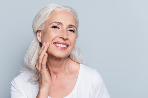 Older woman with long, white hair and clear, beautiful skin touching her cheek