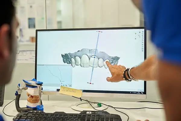 A dentist pointing at a 3D digital teeth model displayed on a computer monitor in a dental lab equipped with modern technology.