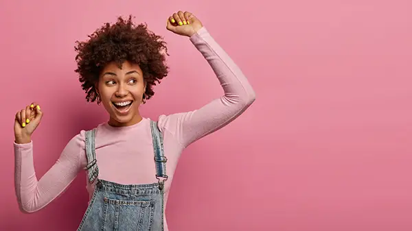 Smiling woman in overalls with a pink background, representing the joy and confidence that comes from good oral health.