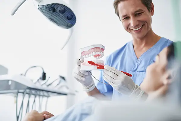 Dentist showing a patient how to use a toothbrush effectively with a dental model during a preventive dentistry appointment.